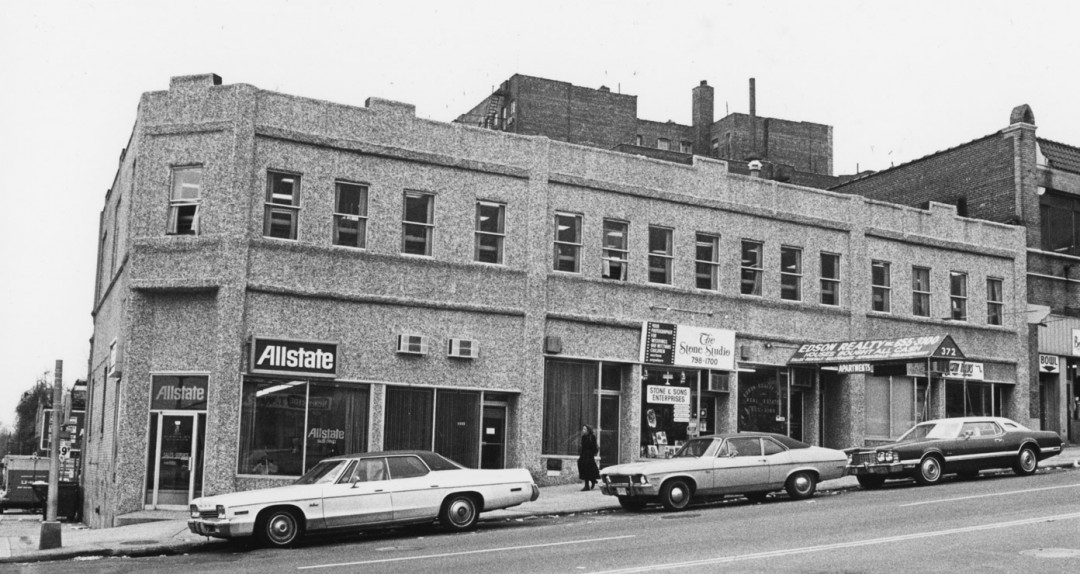 Historical photo of 2-story brick building with 1970's cars along curb
