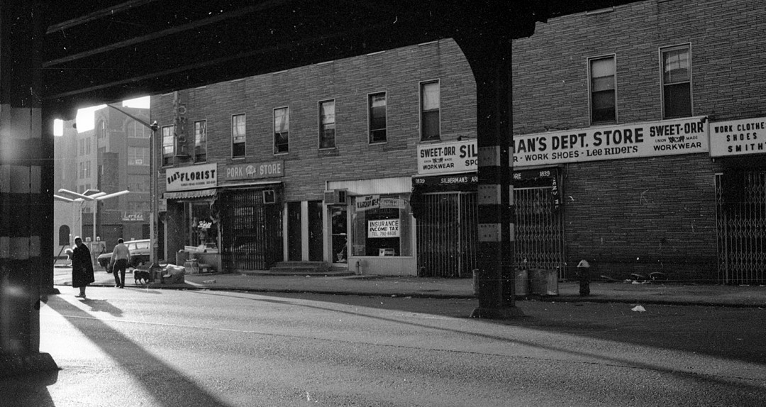 Historical view of brick retail storefronts under elevated train line